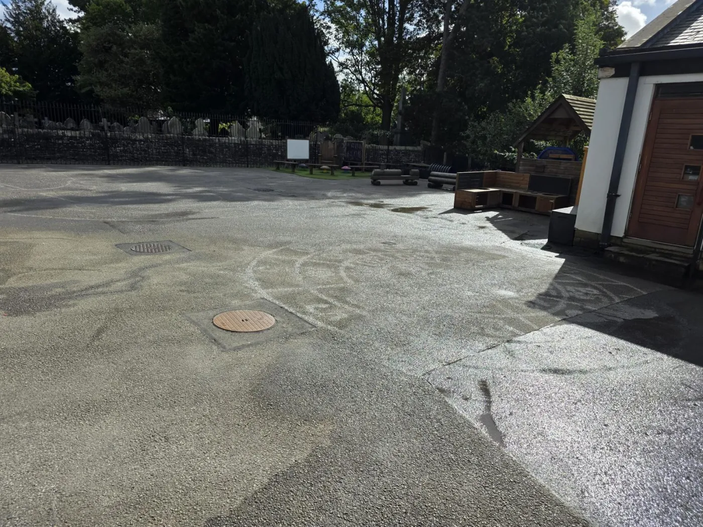 Sunlit playground showing faint ghost rings and a spiral where old markings were ground off the tarmac