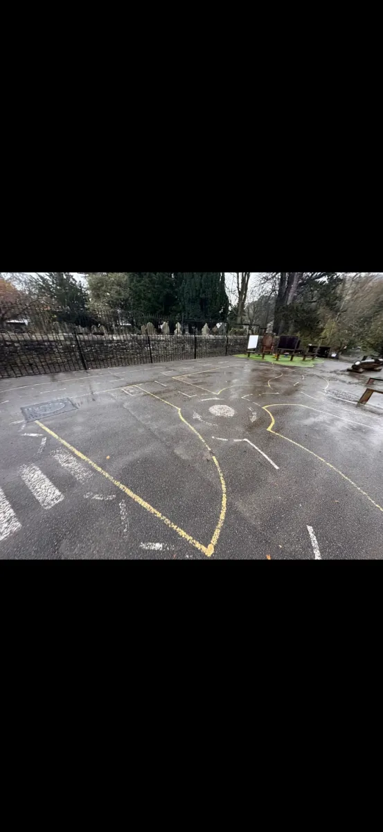 Wet playground where most lines are gone, a yellow curve and faded crossing still showing on the tarmac