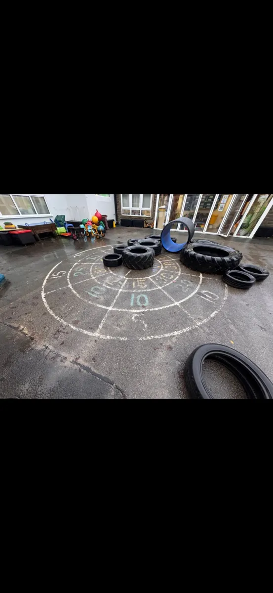 Chalky target circle marked with numbers partly cleared, tractor tyres stacked across the playground surface