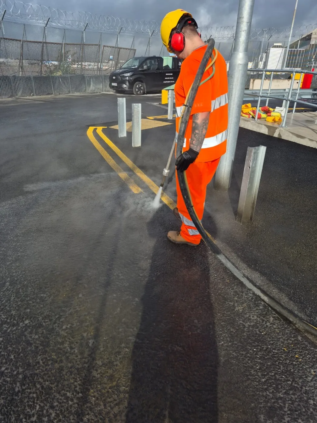 Operator in orange hi-vis blasting a double yellow line off tarmac with a handheld ultra-high-pressure water lance