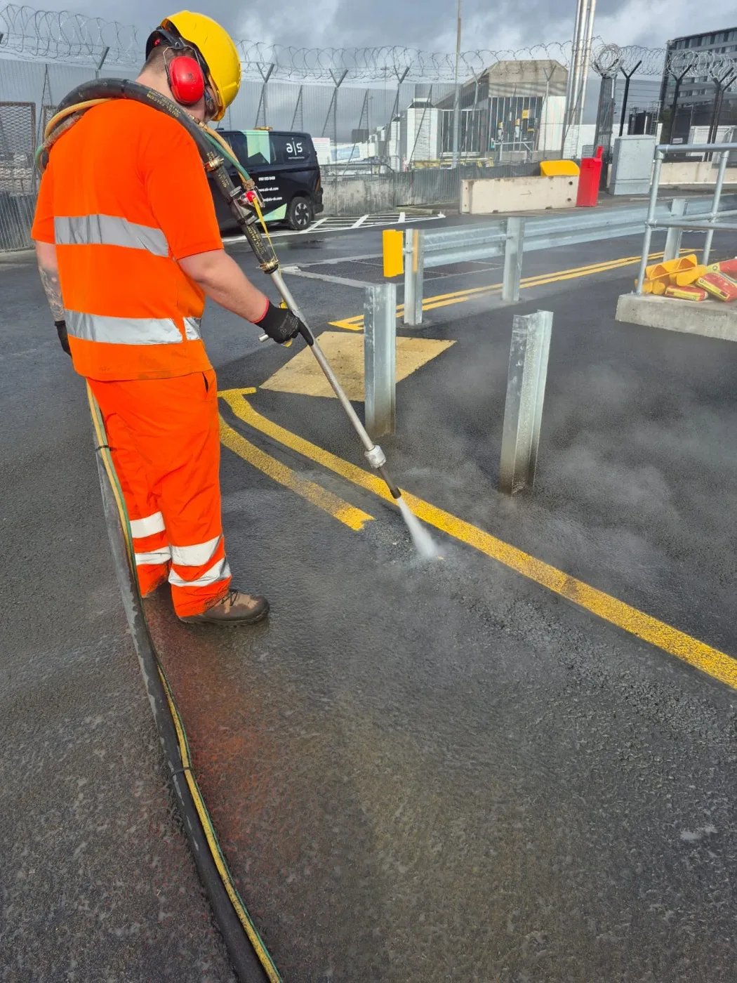 Worker driving a long UHP lance along a yellow line, water spray lifting the paint while the hose coils behind him