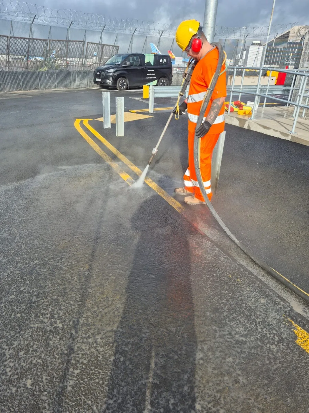 Operator sweeping the water lance across a double yellow marking, loosened paint and spray drifting over the cleared surface