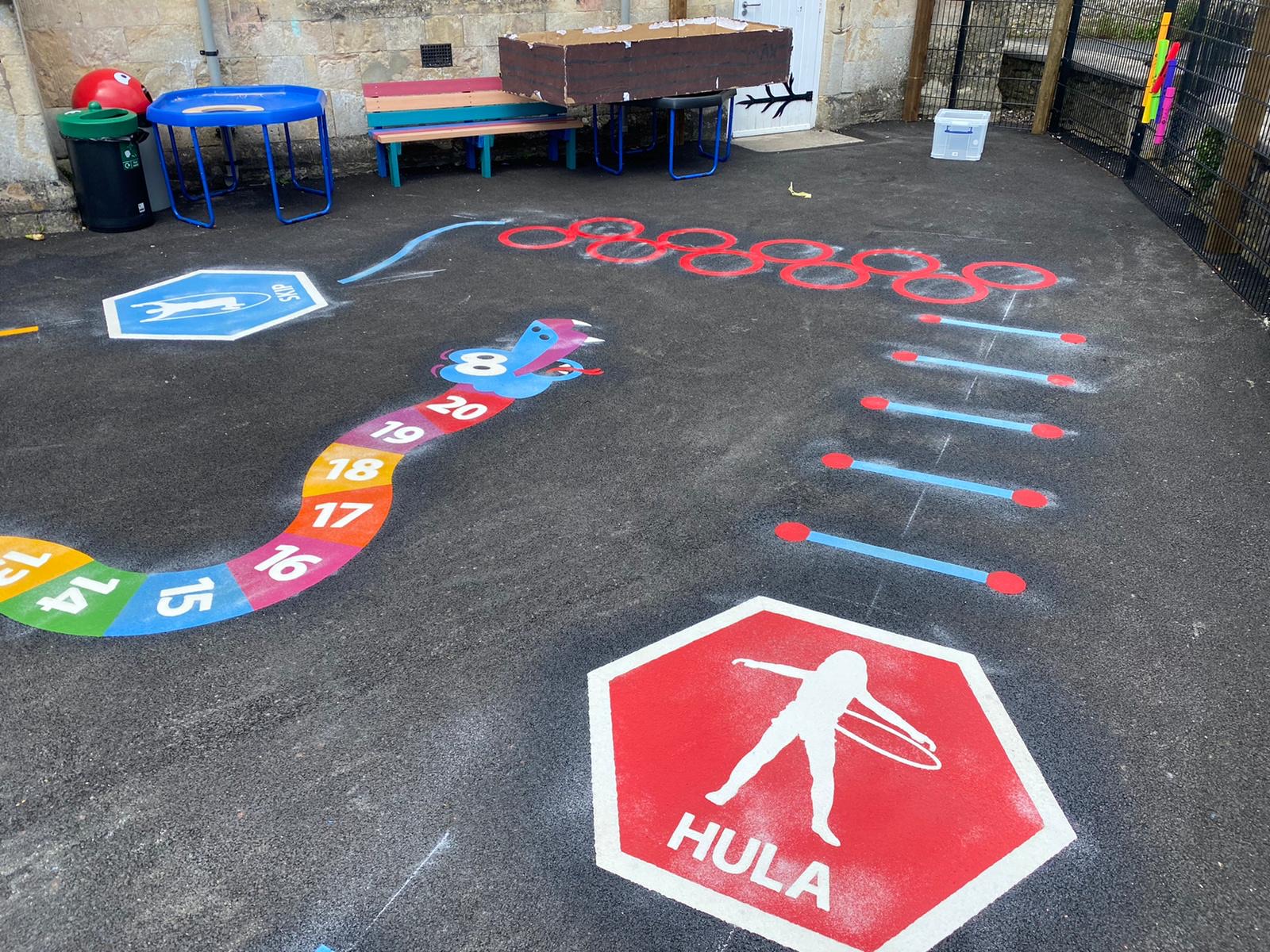 Hula and skip activity hexagons, a number snake and red hoop circle markings on new tarmac in a stone-walled yard