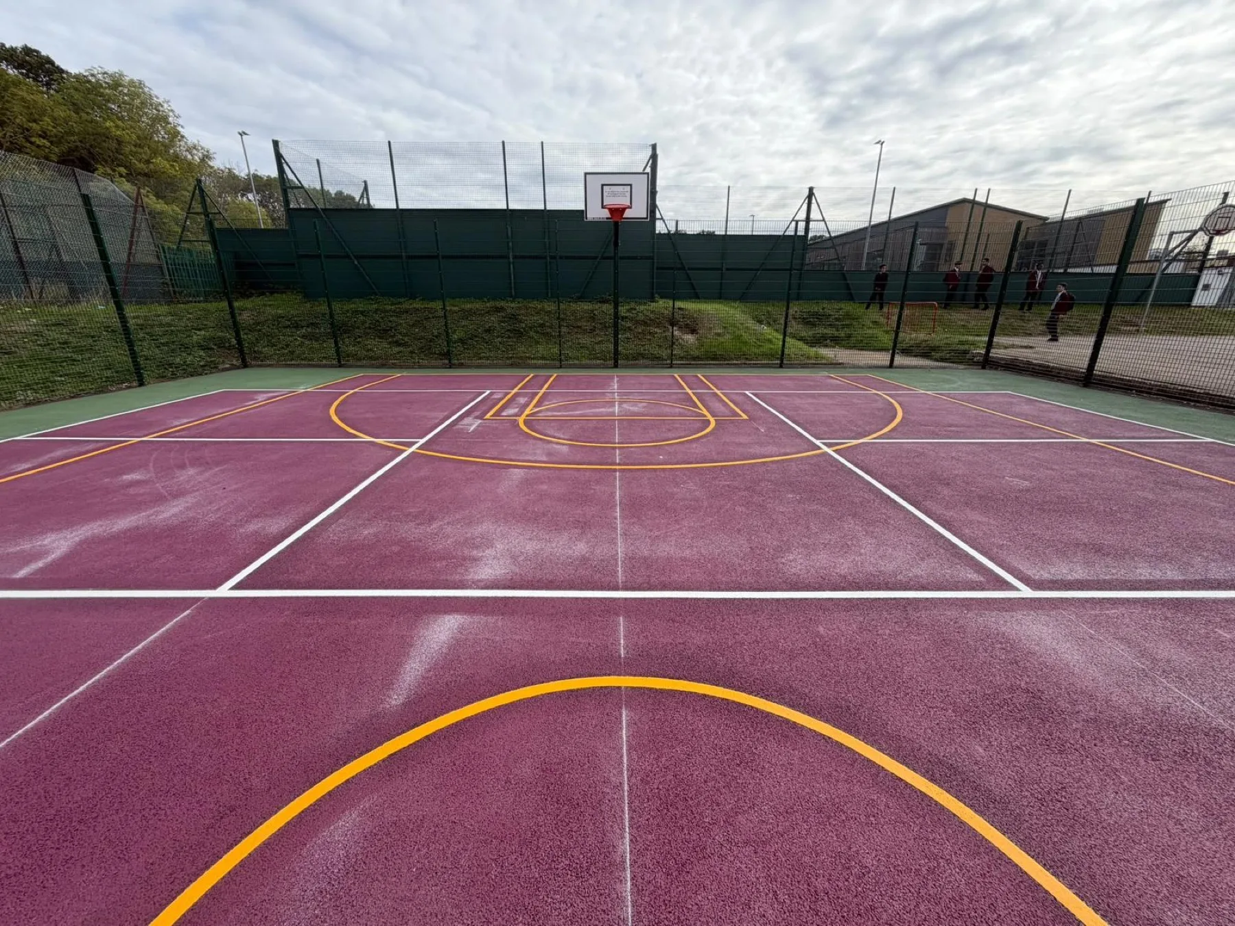A resurfaced purple MUGA with basketball hoops, coloured playing zones and yellow and white court line markings