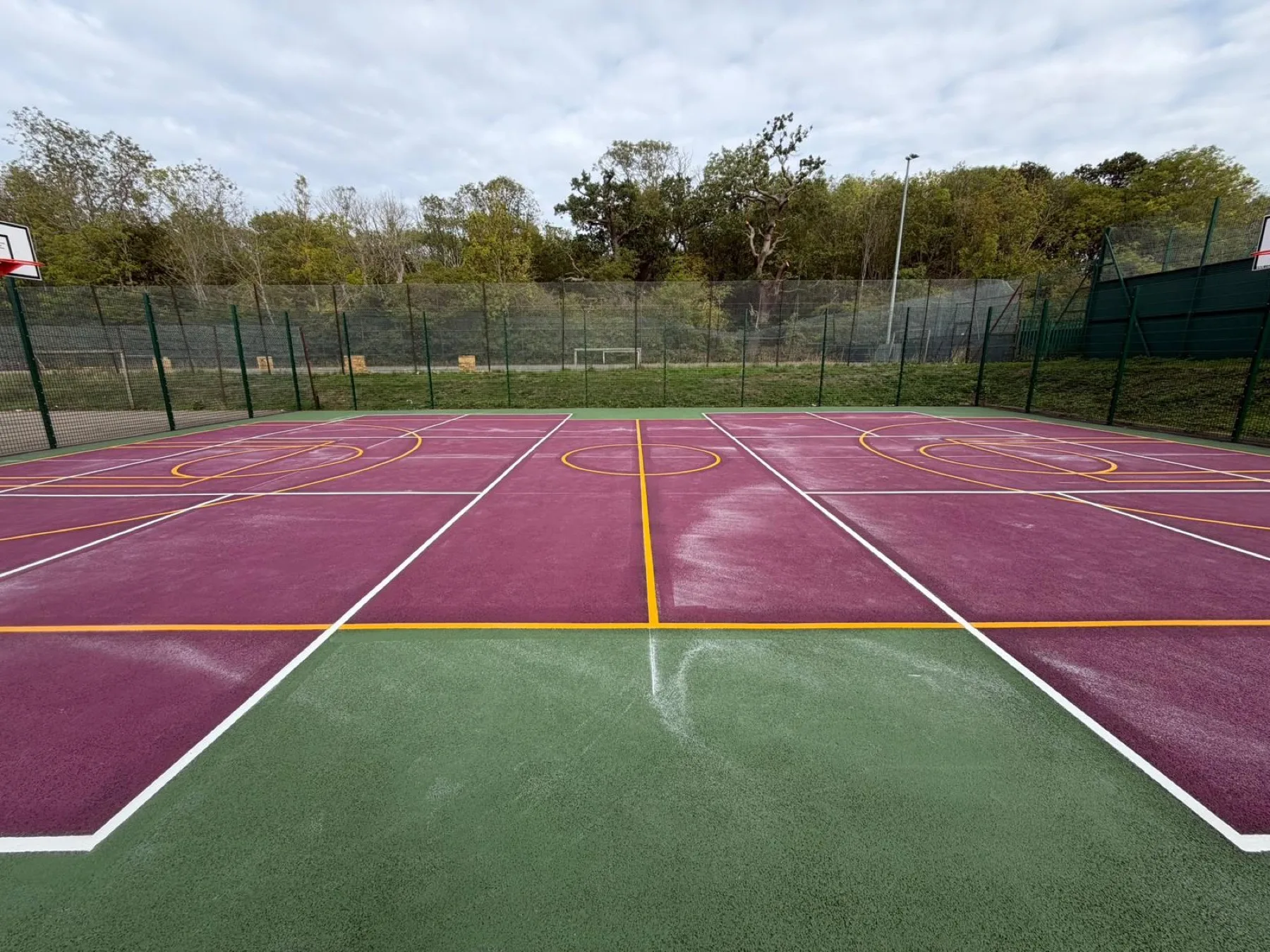A bright, fully coloured multi-use games area with a football goal and netball court lines on a resurfaced purple playing surface